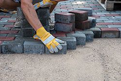 brick mason installing driveway pavers in gray and brown brick tone